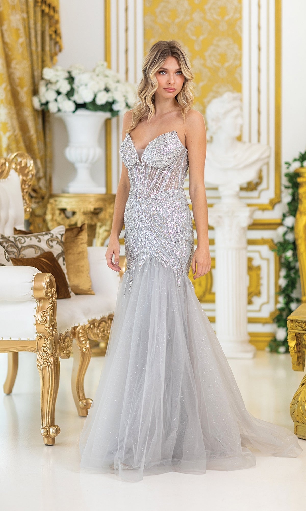 A woman in the Sequin-Bodice Long Prom Dress: Dancing Queen 4468 stands in an ornate room with gold and white decor, featuring a chair, flowers, and a classical statue.